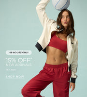 A woman wearing a cream zip-up jacket, red sports bra, red wide-leg track pants, and sneakers poses against a light blue background while balancing a white basketball on her head. She stands on one leg with a playful expression. Text: 48 Hours Only. 15% Off* New Arrivals - T&Cs Apply. Shop Now