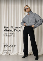 A woman in black All Day Active Midrise Pants styled with an oversized grey checked zip-up jacket, sunglasses and black loafers, against a soft neutral curtain backdrop.
Text: Your Wardrobe's Missing Piece. All Day Active Midrise Pants. Take $30 Off* T&Cs apply - Shop Now