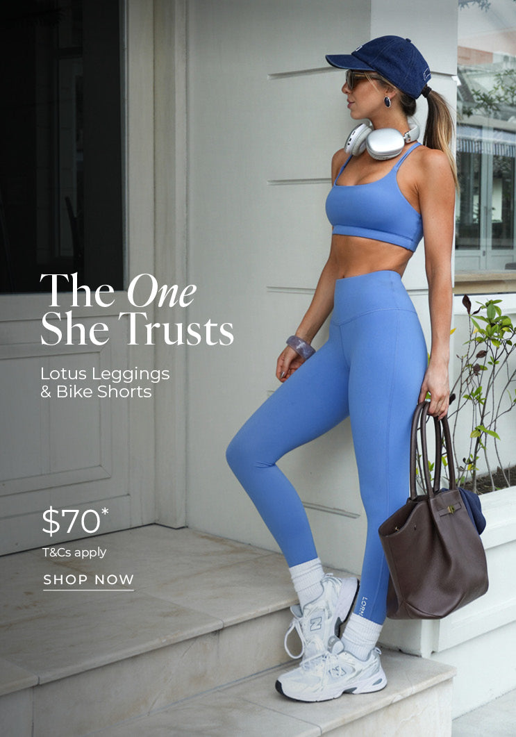 A woman stands on a marble step in a periwinkle blue Lotus sports bra and matching leggings, wearing a navy cap, white sneakers and carrying a brown handbag. Text: The One She Trusts. Lotus Leggings & Bike Shorts $70* T&Cs apply - Shop Now