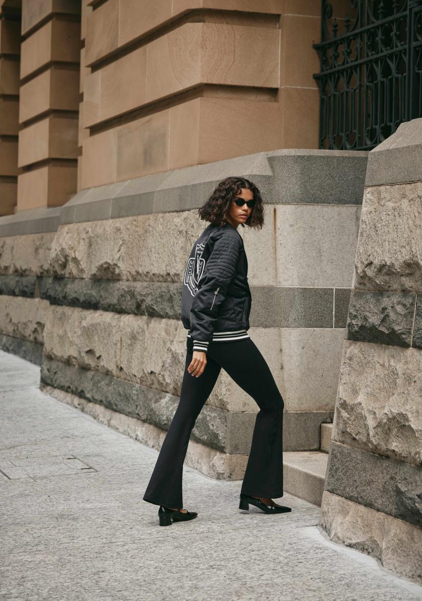 Model wearing black jacket and black leggings standing in front of concrete pillars