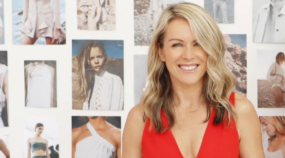 Photo of Lorna Jane Clarkson wearing a red top standing in front of a wall with photos