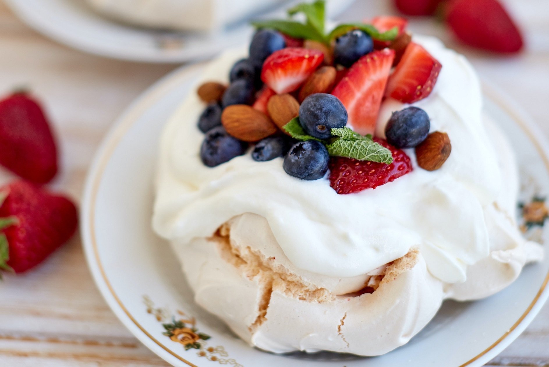 vegan pavlova topped with strawberries, almonds, blueberries and mint leaves