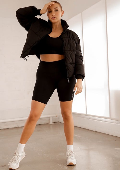 auburn woman wearing black 19cm bike shorts, sports bra and a puffer jacket