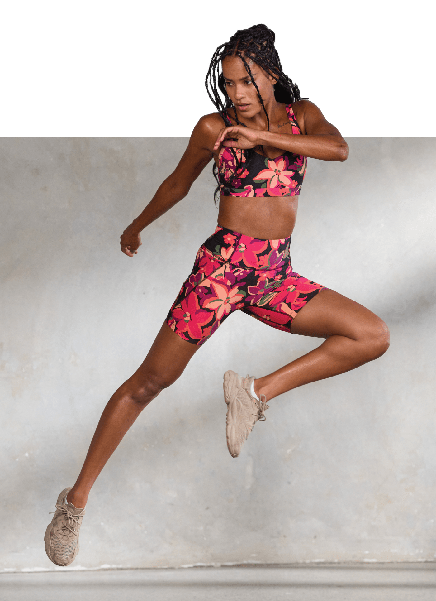 Front image of a model jumping in the air wearing pink floral sports bra and pink floral bike shorts.