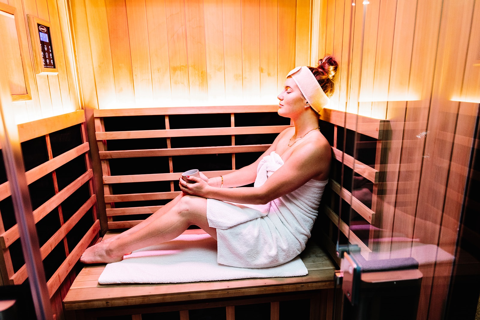 Woman sitting in infrared sauna wrapped in towel at Kailo Medispa