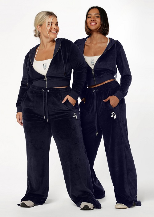 Two models wearing matching blue velour tracksuit sets