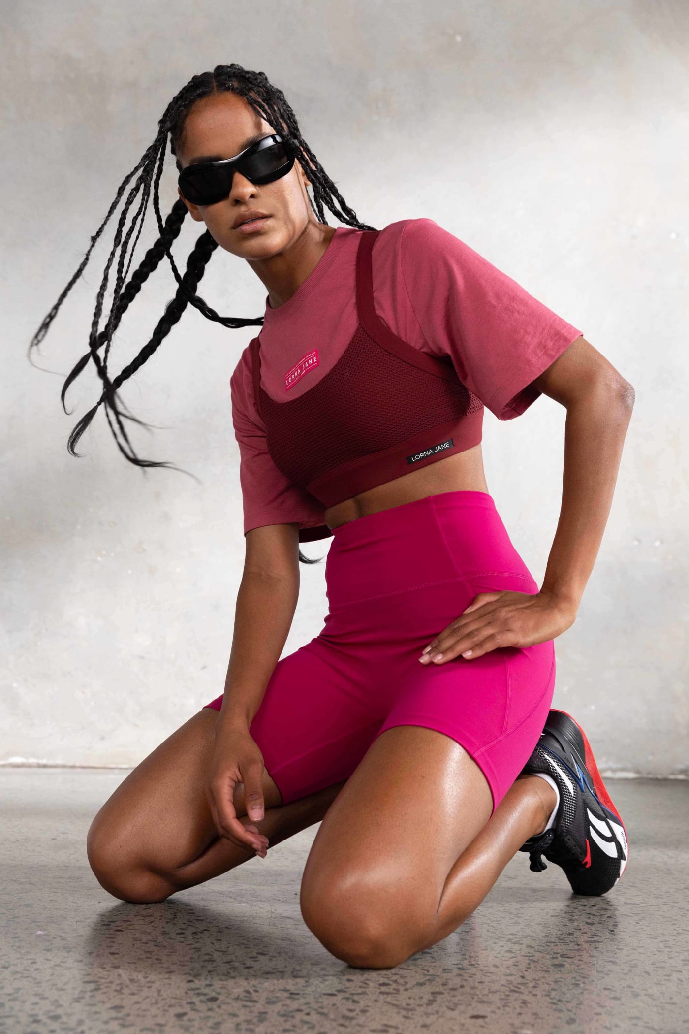 Front shot of a model on her knees wearing pink Lorna Jane activewear and sunglasses.