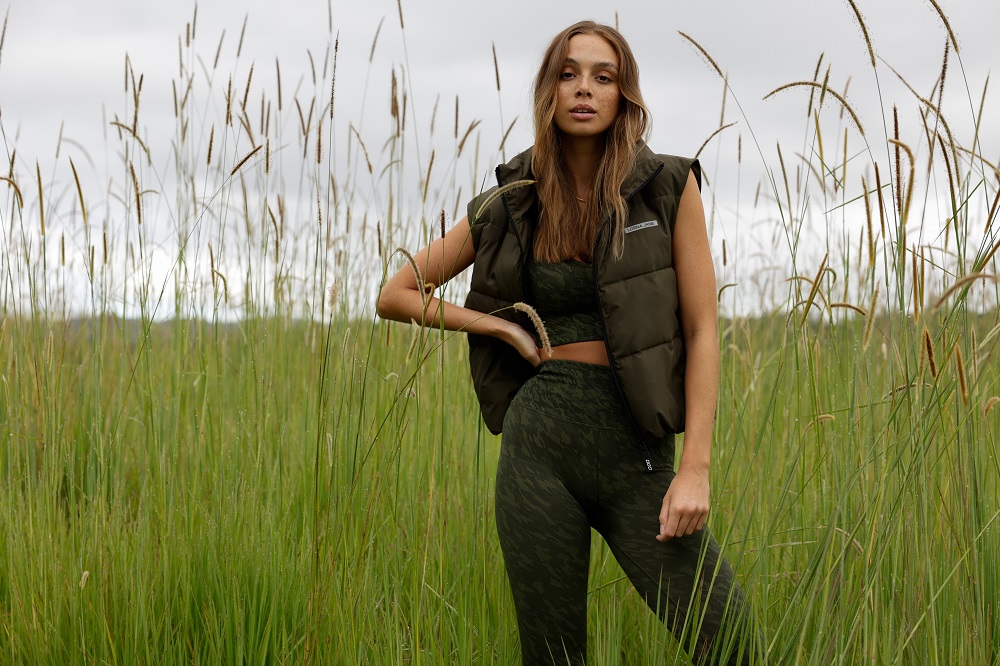 woman wearing army green puffer jacket vest and army print leggings and sport bra