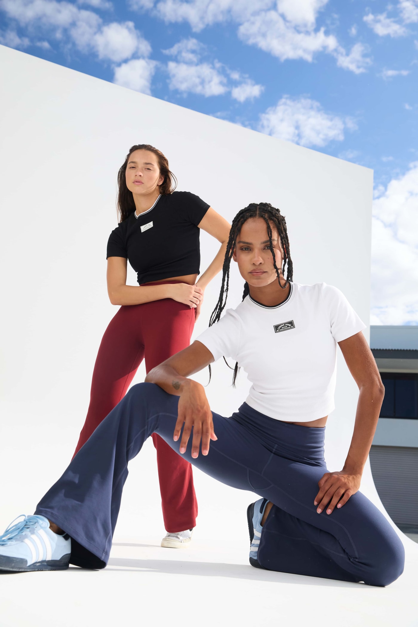 Two models wearing Lorna Jane activewear flares in blue and sepia colours. One model is crouching down.
