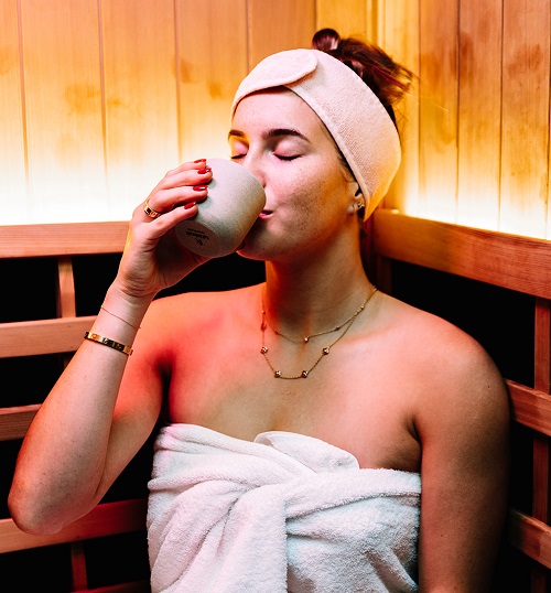 woman sitting in infrared sauna at Kailor Medispa drinking from mug