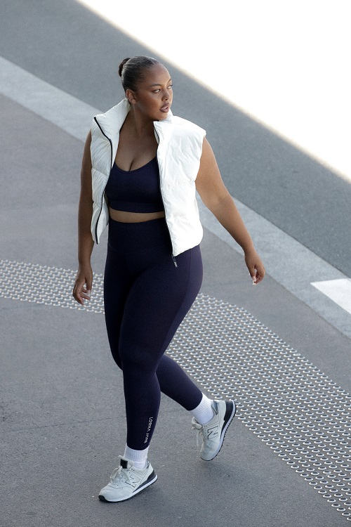 a woman wearing black full length leggings, a black sports bra and a white cropped puffer vest