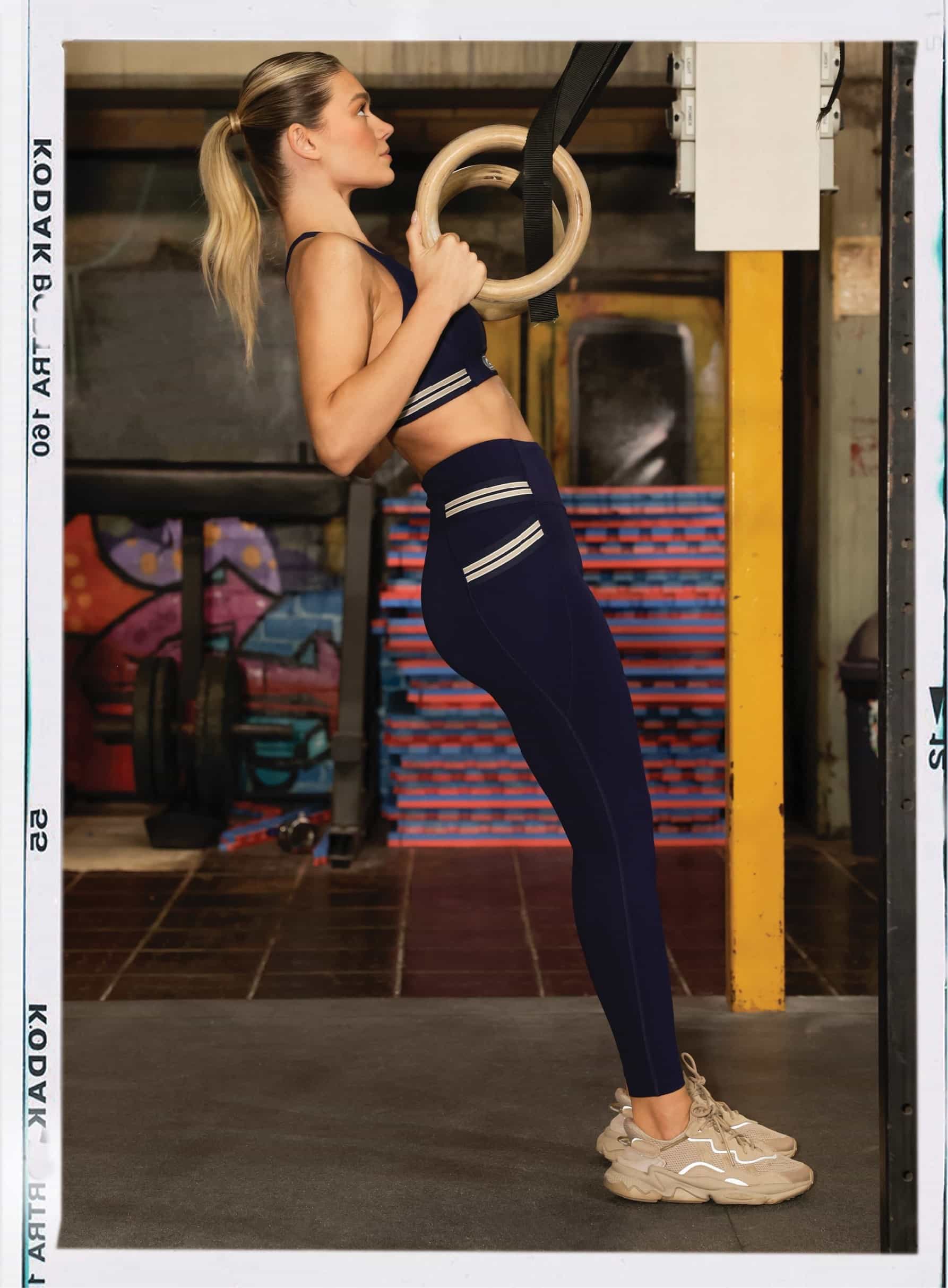 Side shot of model doing ring rows wearing matching navy sports bra and leggings with cream detailing on pockets