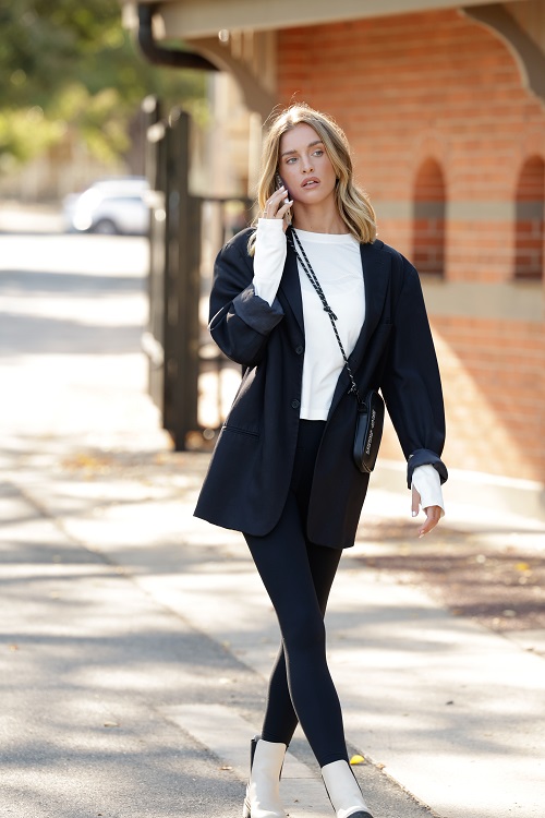 woman wearing black leggings, a white oversized long sleeve tee and oversized black blazer and a black crossbody bag